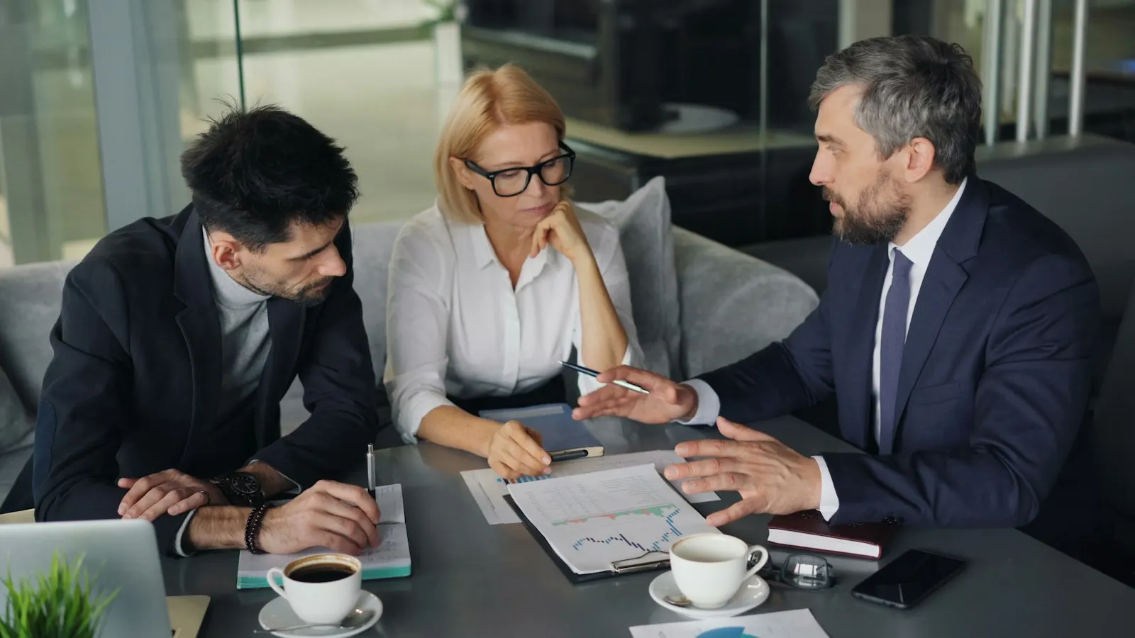 Three people talking through plans and paperwork over coffee at an office table